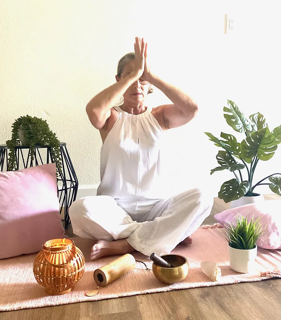 Seated meditation with hands raised in prayer beside a singing bowl at Serenity Hot Yoga