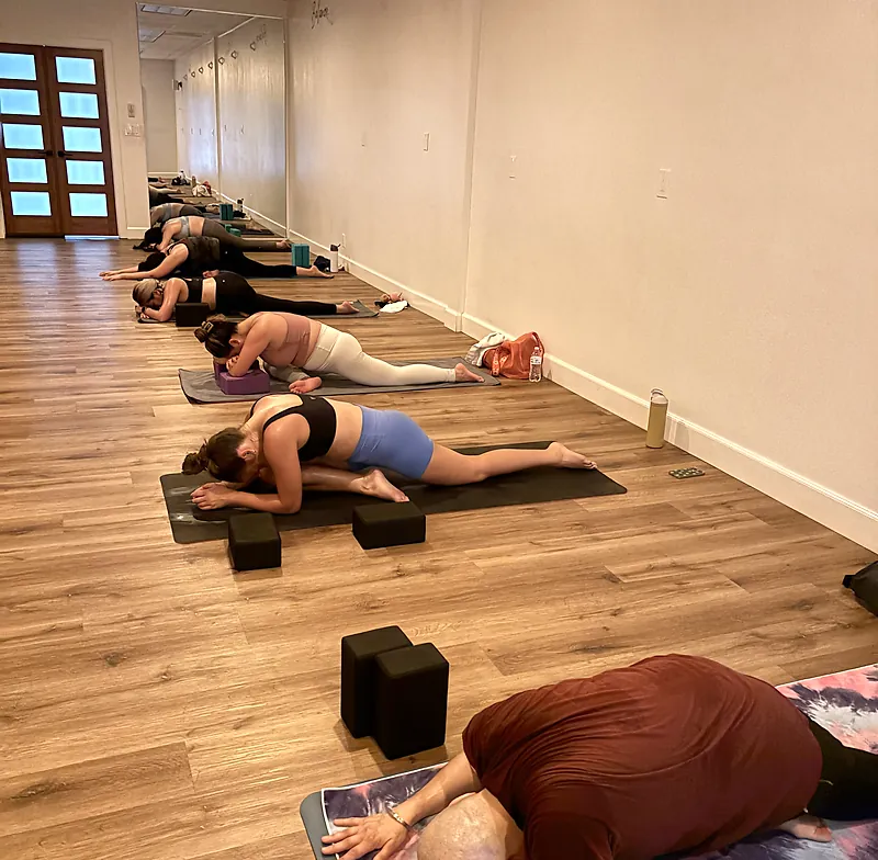 Students folding forward in pigeon pose during a non-heated class at Serenity Hot Yoga